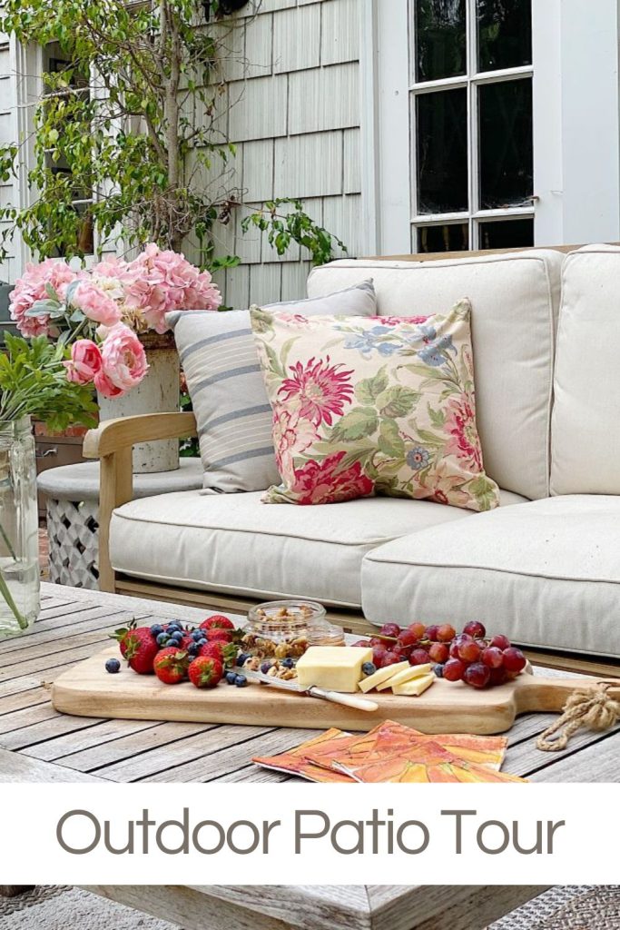 Backyard patio with wood furniture with white cushions and floral pillows and fresh flowers.
