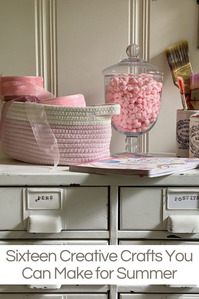 A craft room with a basket full of pink ribbons, a glass jar with pink fringe, and a book about crafting.