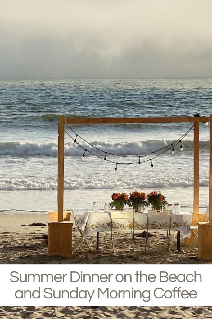 A dinner on the beach with a wood frame, beautiful table and three centerpieces.