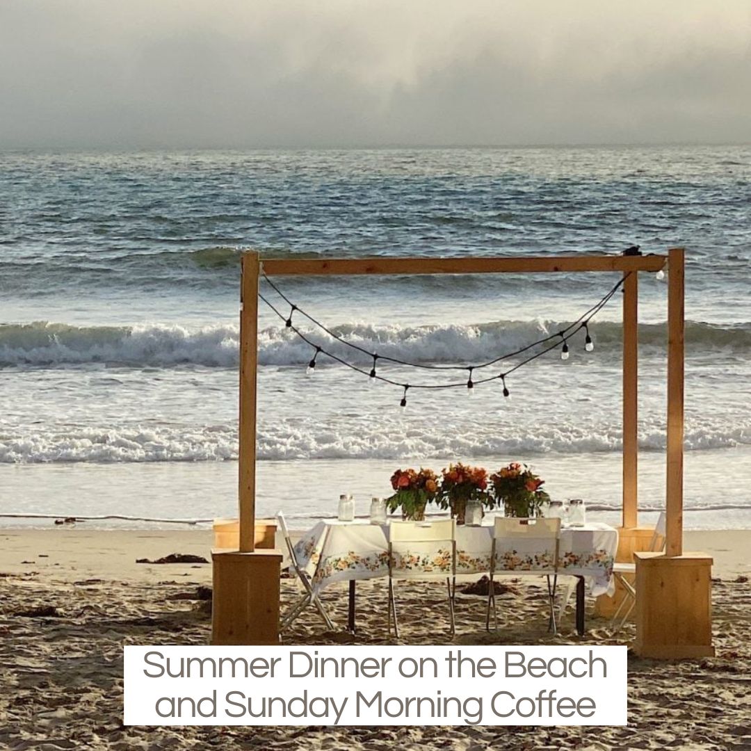 A dinner on the beach with a wood frame, beautiful table and three centerpieces.