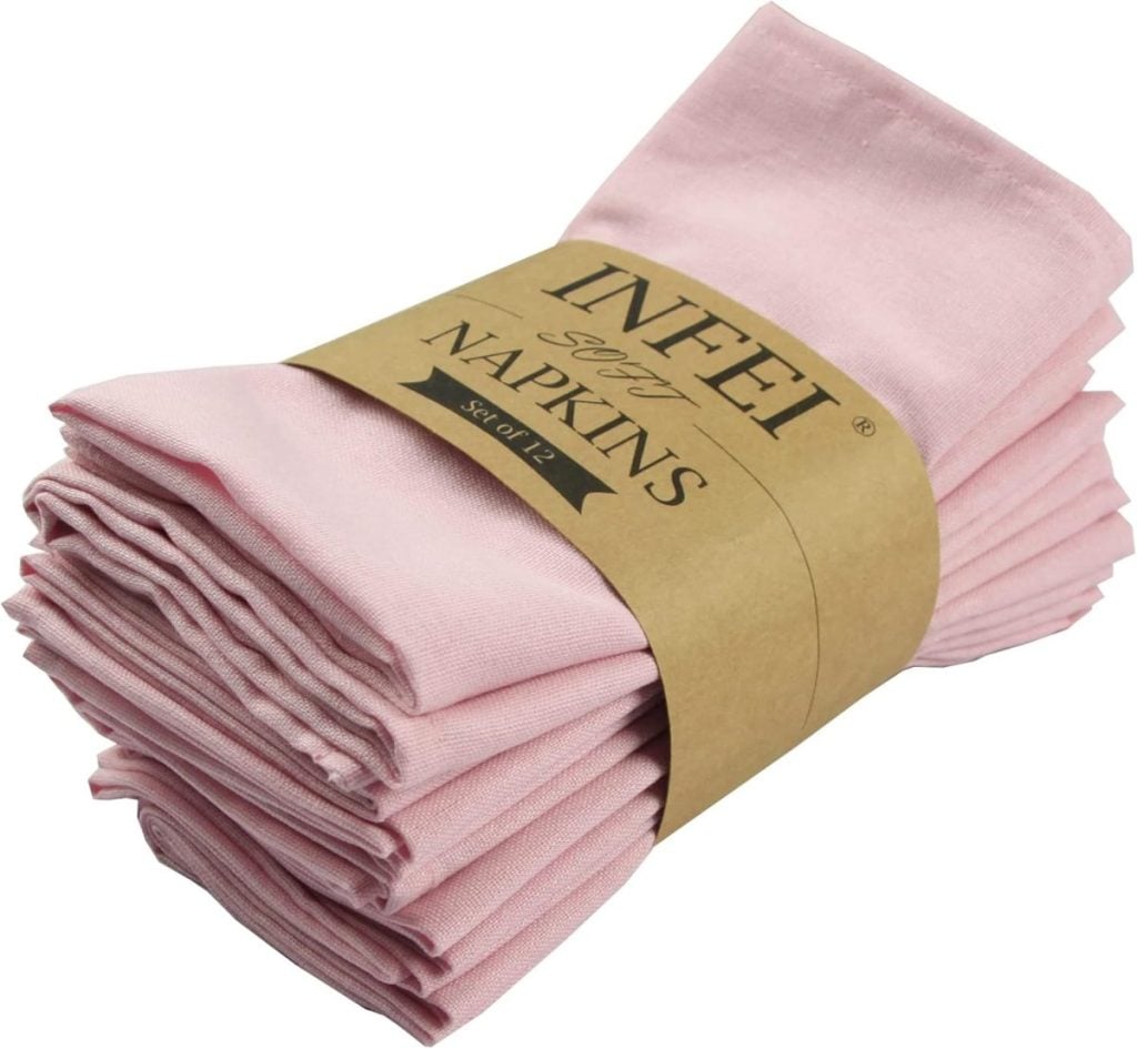 A stack of folded pink cloth napkins, bundled together with a brown paper band labeled "INFEI Soft Napkins Set of 12," perfect for your fall table decor ideas.