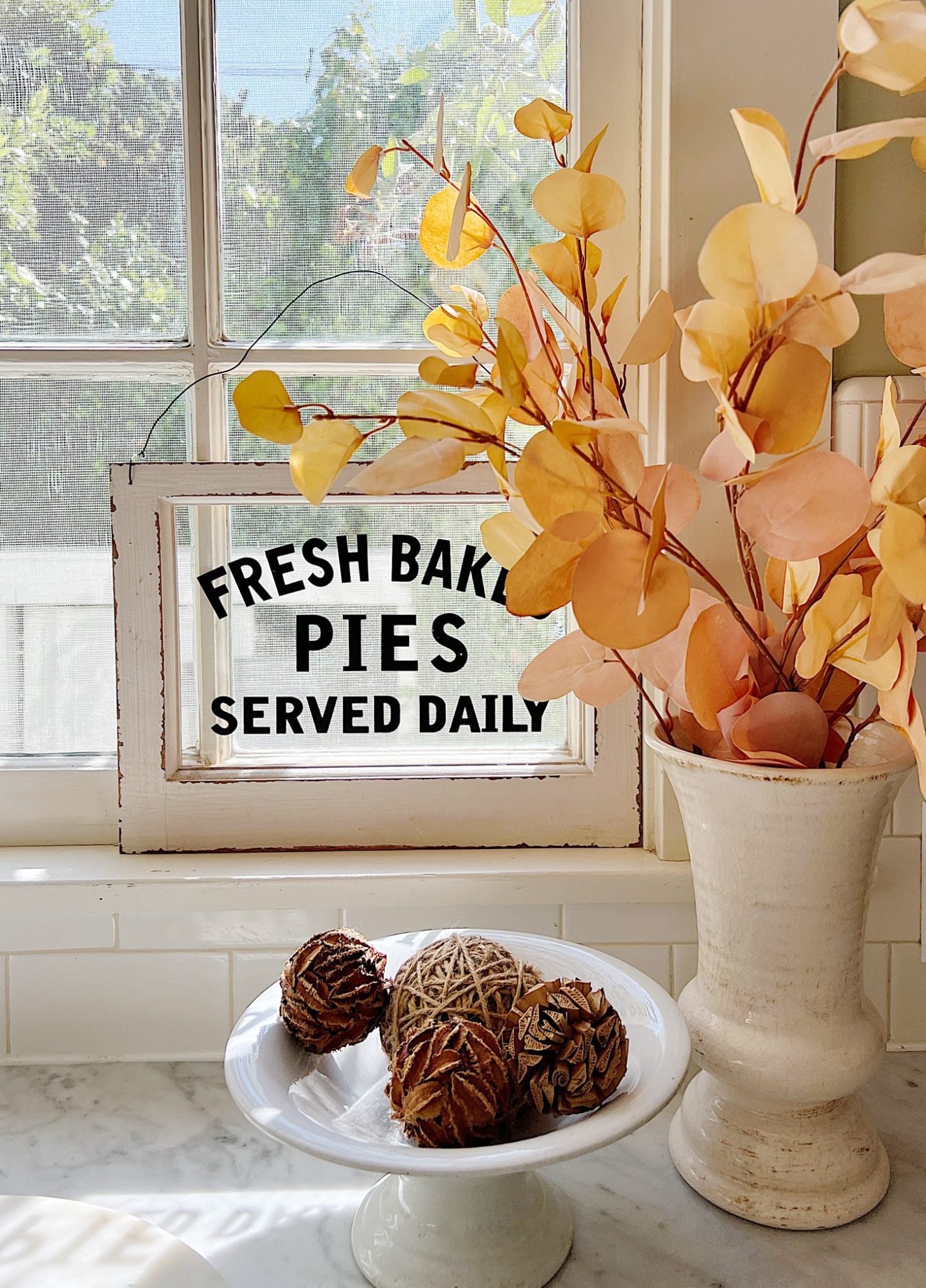 A white kitchen with an island and rattan barstools decorated with fall decor.