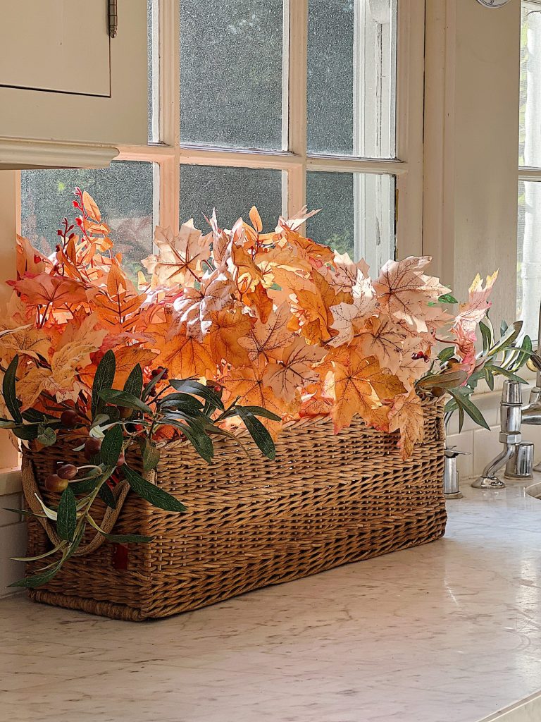 A white kitchen with an island and rattan barstools decorated with fall decor.