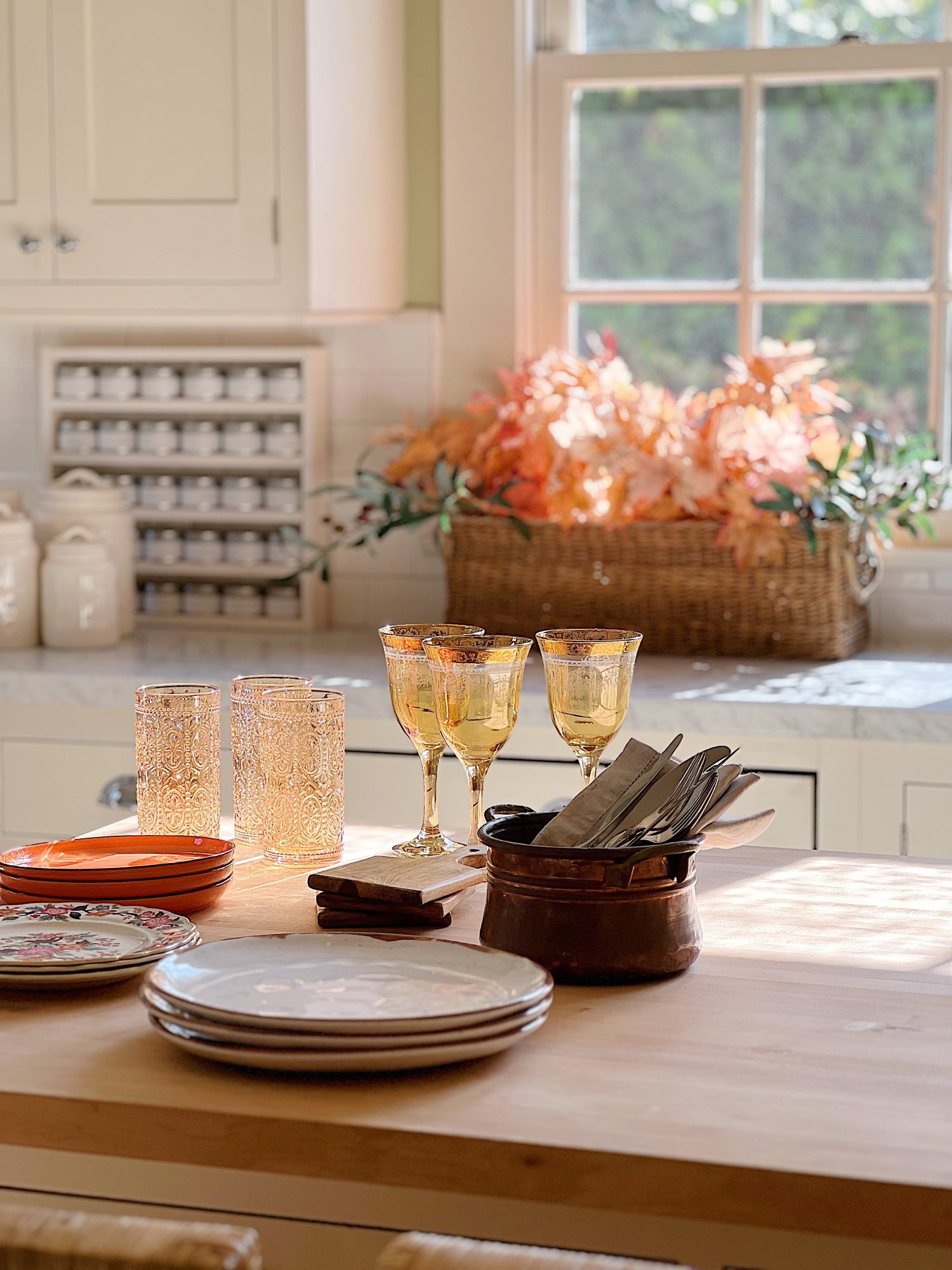 A white kitchen with an island and rattan barstools decorated with fall decor.