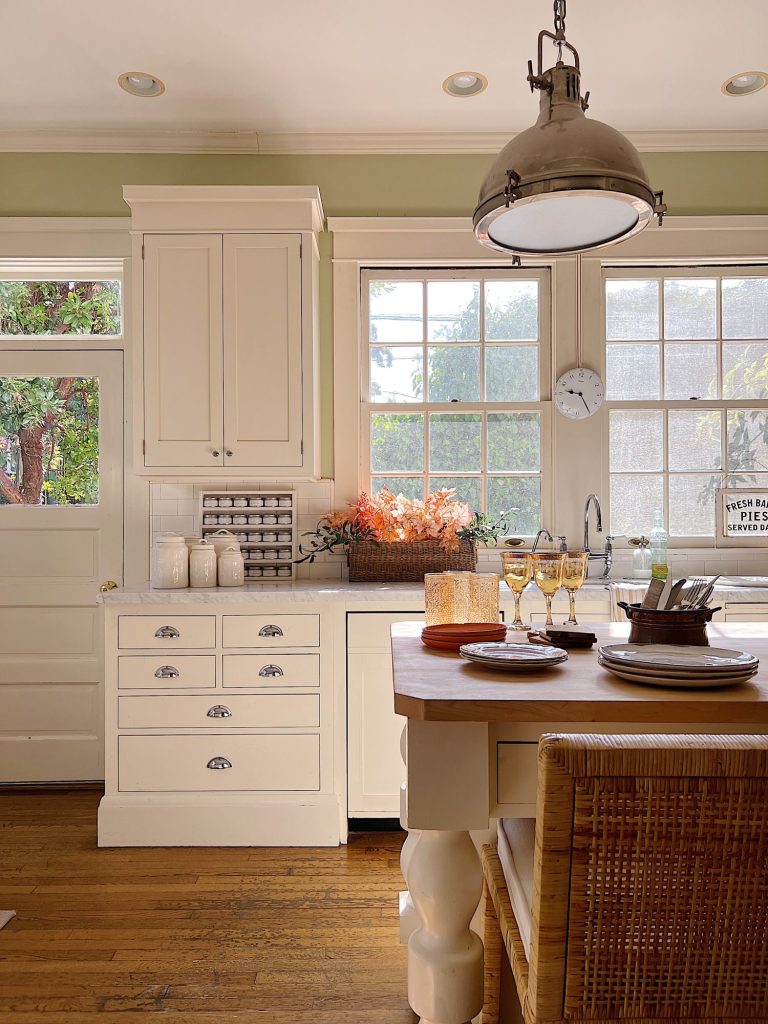 A white kitchen with an island and rattan barstools decorated with fall decor.