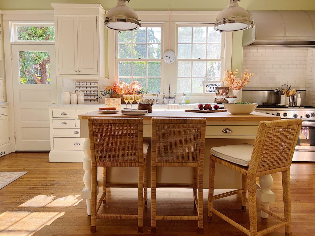 A white kitchen with an island and rattan barstools decorated with fall decor.