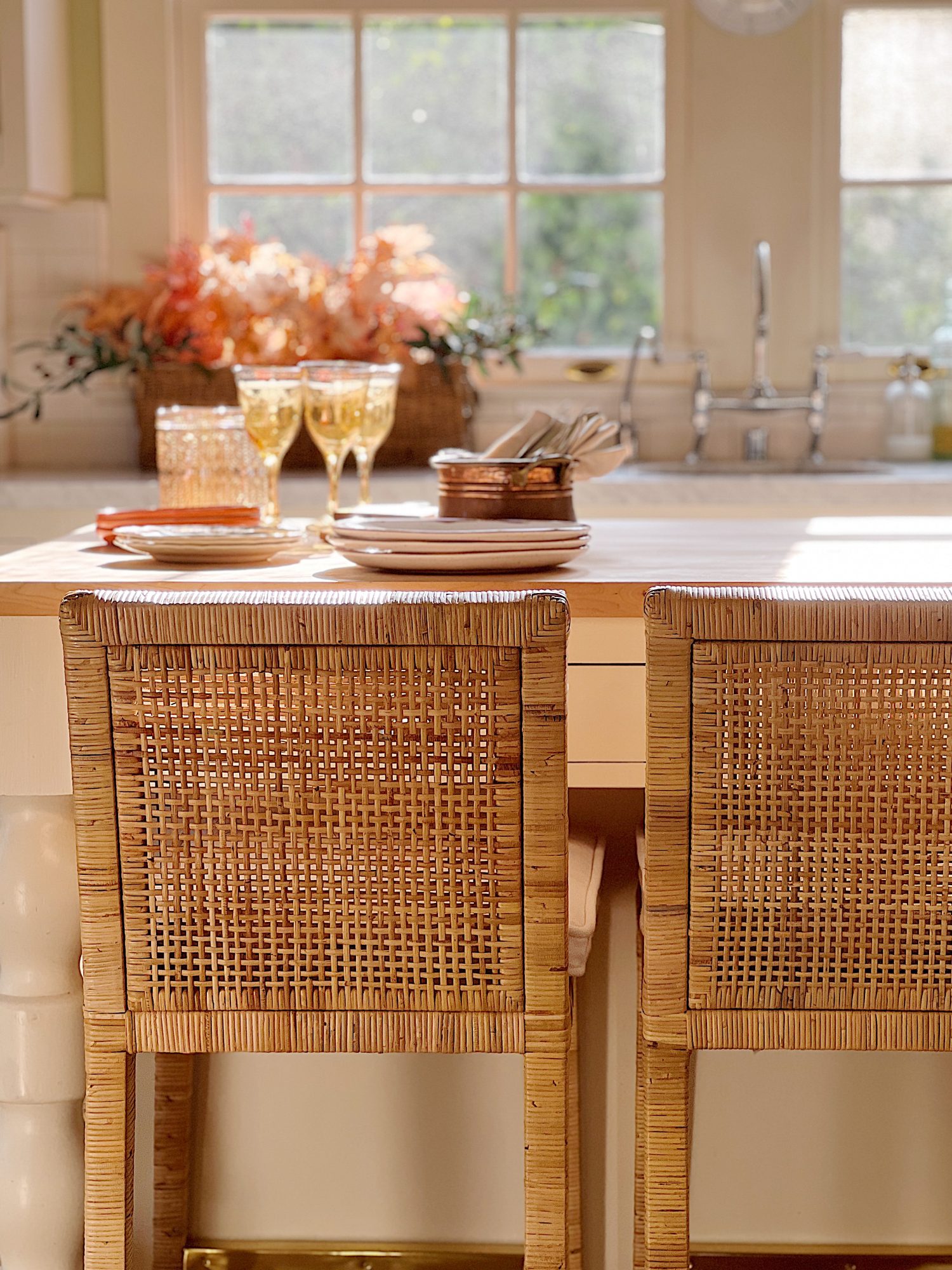 A white kitchen with an island and rattan barstools decorated with fall decor.