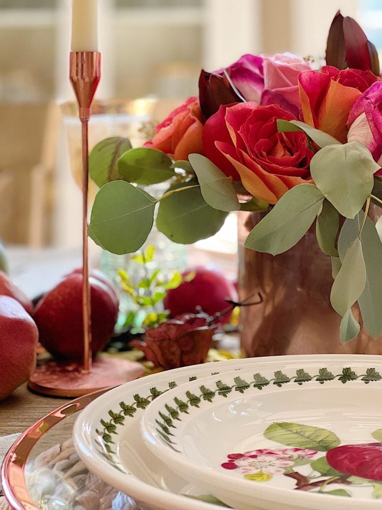 A table set for fall with roses, fall fruits, and tableware.