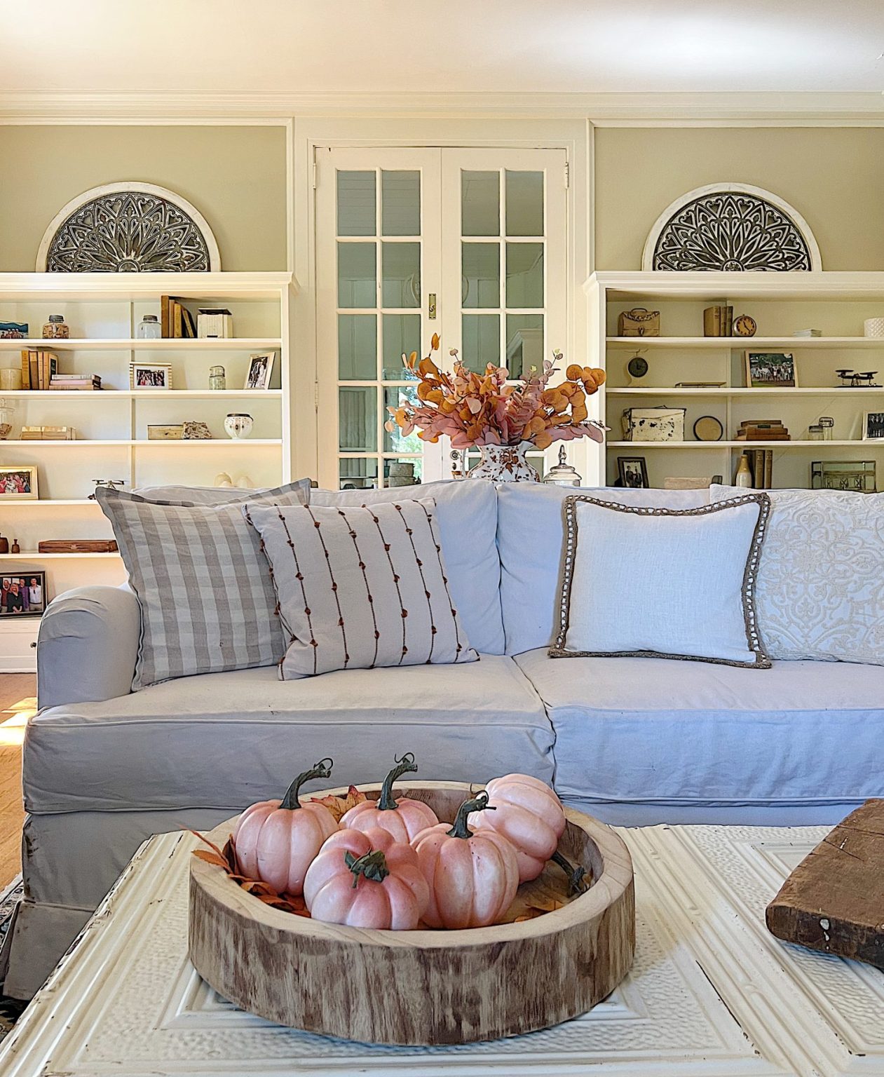 A neutral living room styled for fall with apricot, pink, and light orange florals and decor.