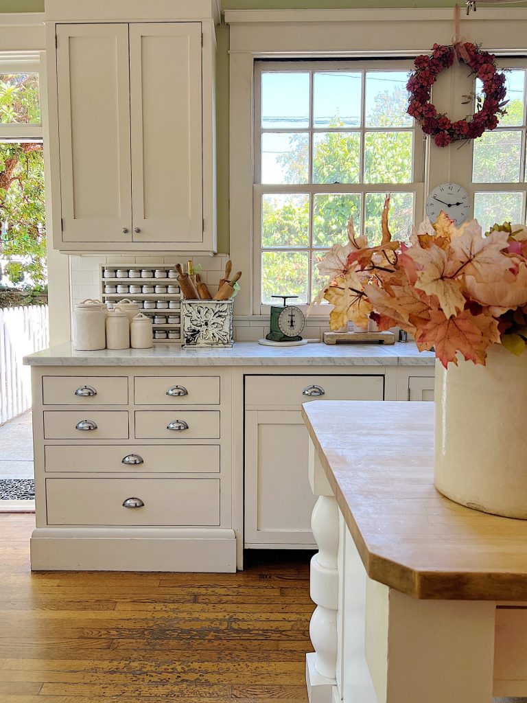 A white farmhouse kitchen with white cabinets, fall decor, and a butcher block island.