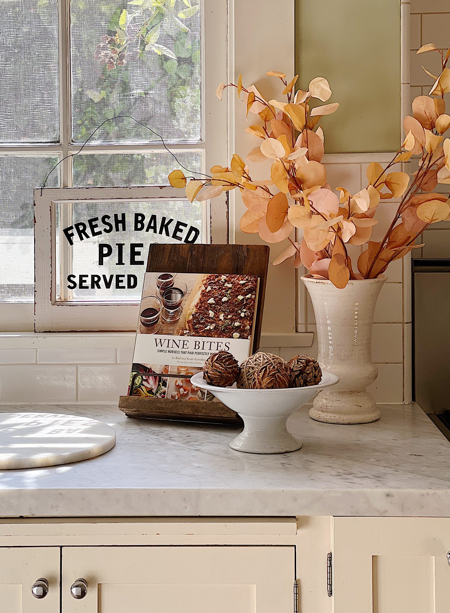 A white kitchen with an island and rattan barstools decorated with fall decor.