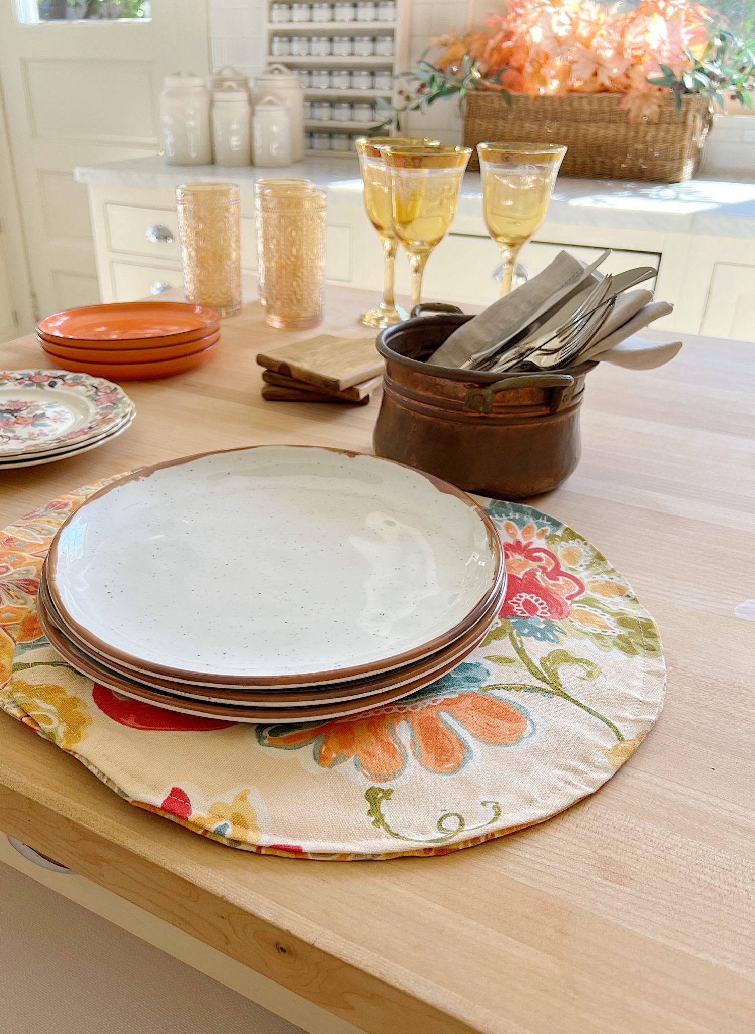 A white kitchen with an island and rattan barstools decorated with fall decor.