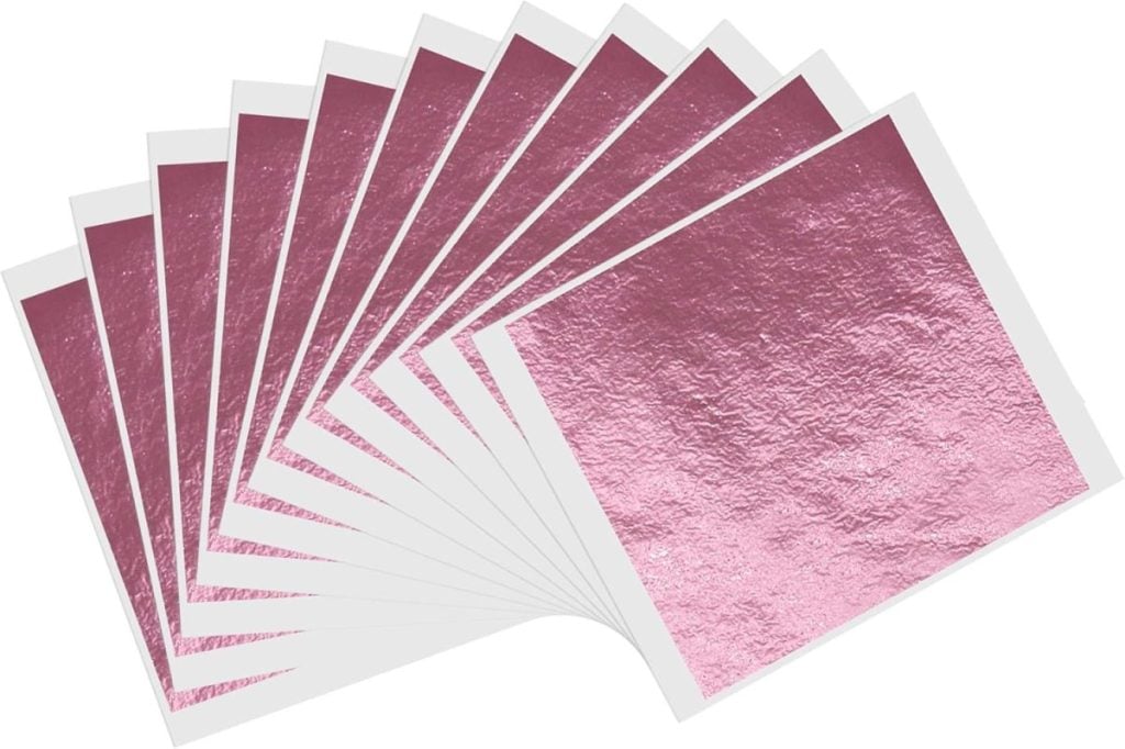 A fan of ten metallic pink foil sheets, each partially lifted at one corner like falling leaves in autumn, displayed against a white background.