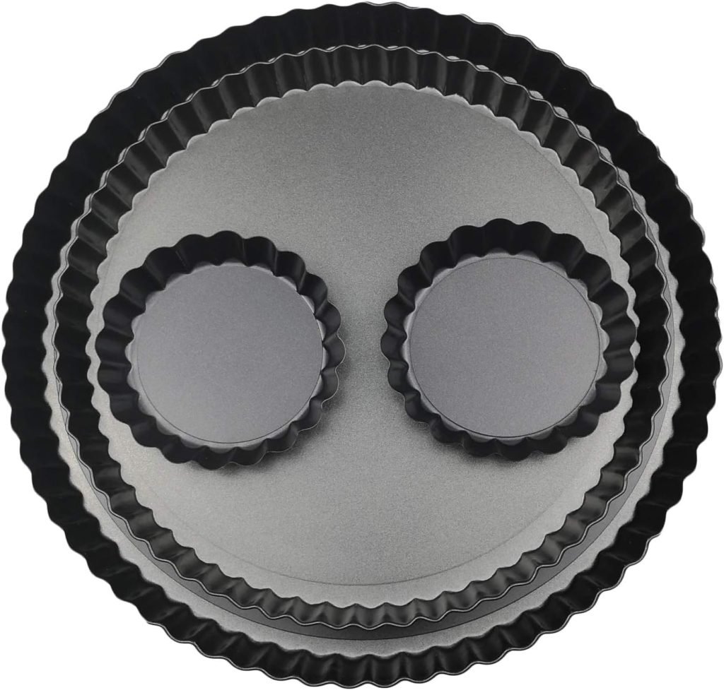 Five stacked fluted tart pans, reminiscent of a smiley face, range from large to small, eagerly awaiting the creation of a pear and cranberry tart.