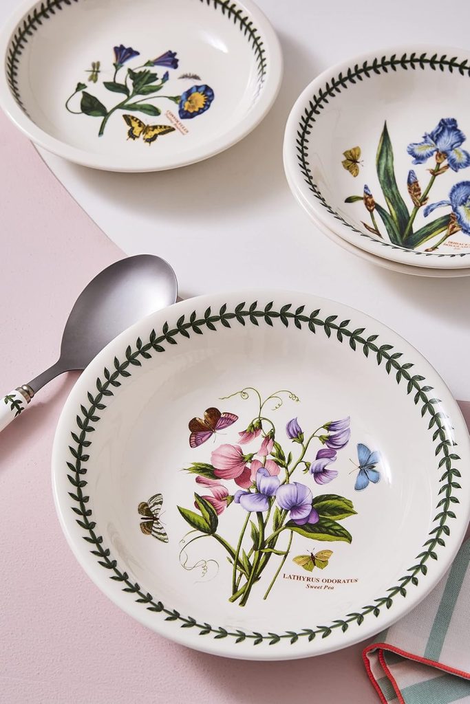 Three white ceramic protein bowls with botanical and butterfly illustrations sit on a light pink and white surface, next to a metal spoon with a patterned handle.