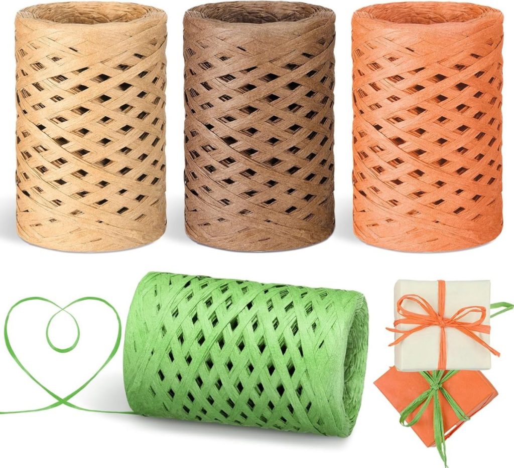 Four spools of raffia twine in beige, brown, orange, and green. A piece of green twine forms a heart shape while some wrappings are shown with the twine tied as bows. Perfect for adorning fall pumpkins.