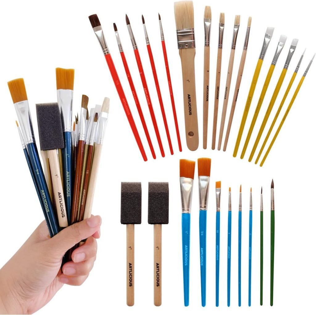 A hand holding various paintbrushes with more paintbrushes arranged in sets on a white background, reminiscent of the hues found in wreaths for fall.