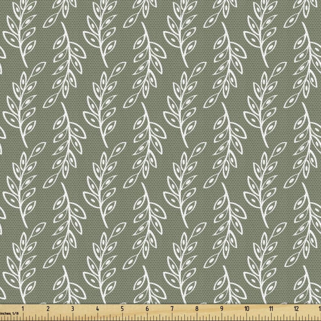 A fabric with a repeated white leaf pattern on a muted green background, accented with subtle fall pumpkins, shown with a measuring ruler at the bottom for scale.