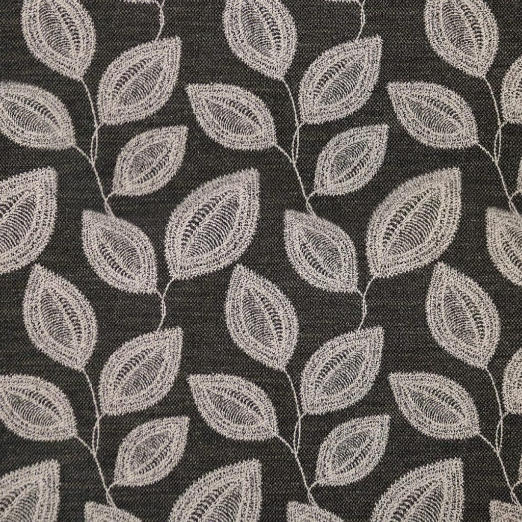 A close-up image of a black fabric with a repetitive pattern of white embroidered leaves, subtly accented by small fall pumpkins.