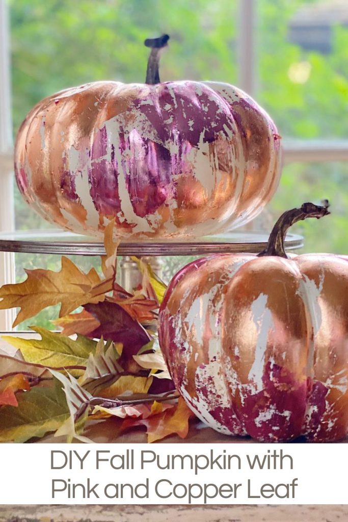 Two white pumpkins covered in orange and pink metal leaf sitting in front of a window.
