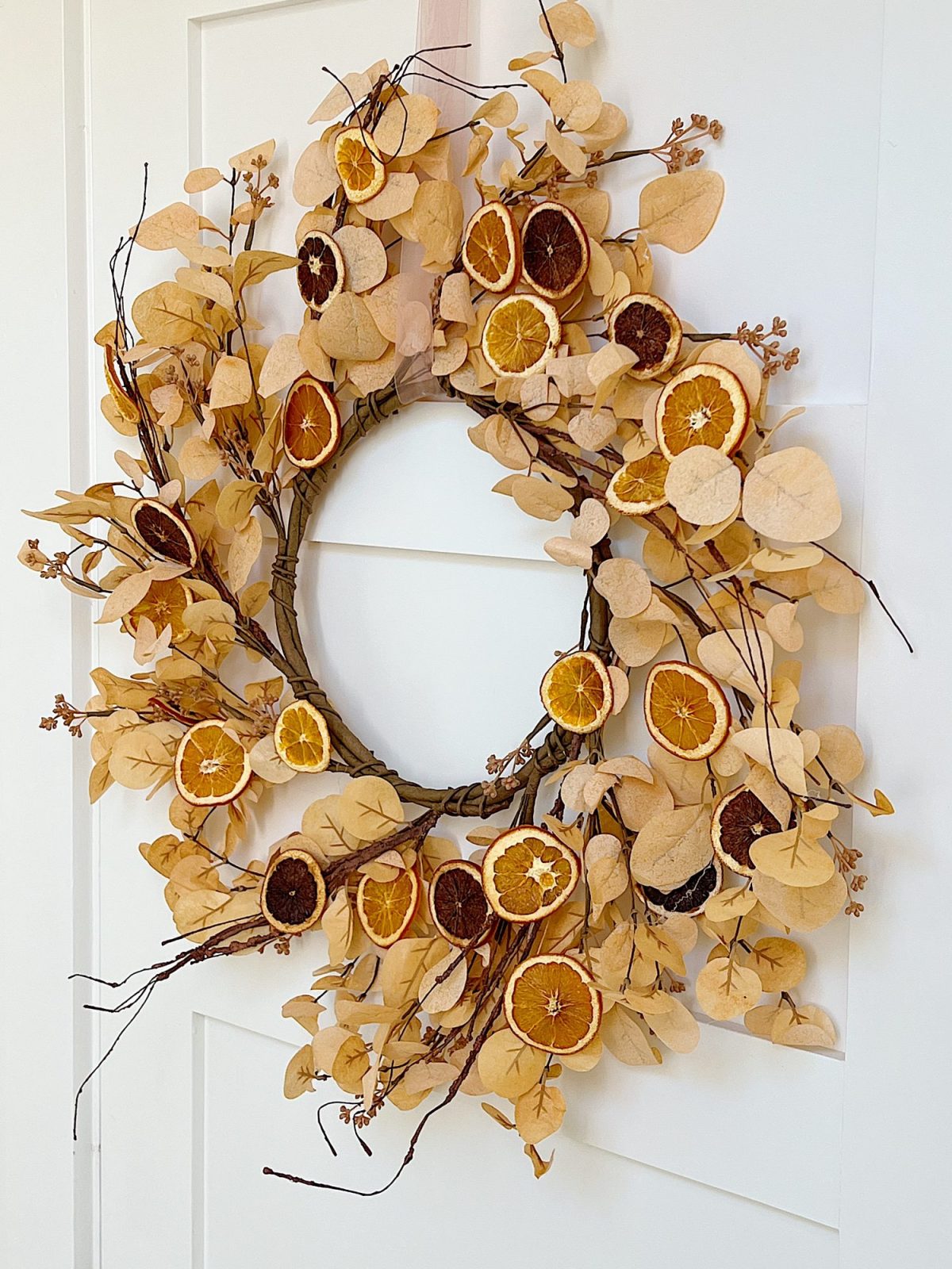 A DIY Halloween wreath made with a eucalyptus wreath and dried orange slices.