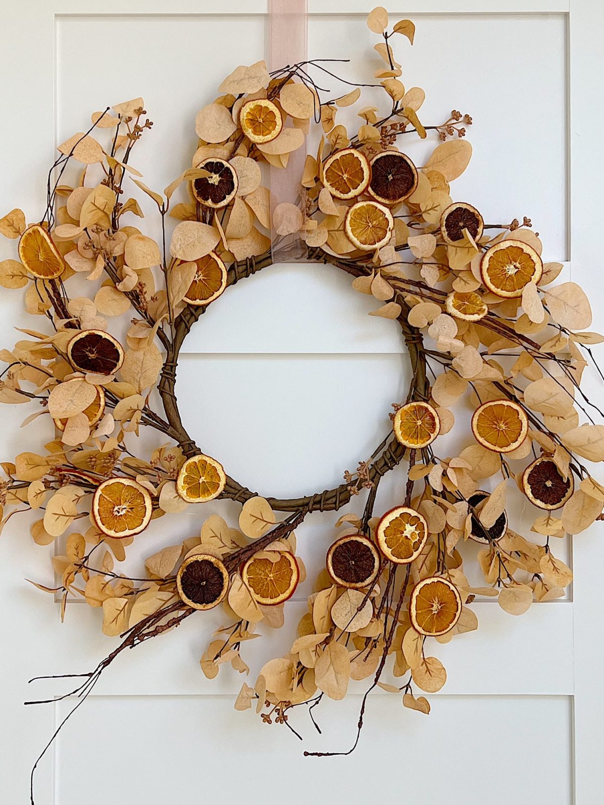 A DIY Halloween wreath made with a eucalyptus wreath and dried orange slices.