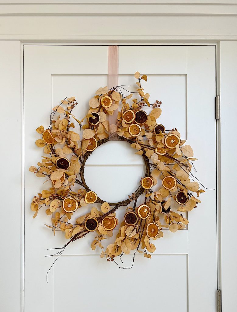 A DIY Halloween wreath made with a eucalyptus wreath and dried orange slices.