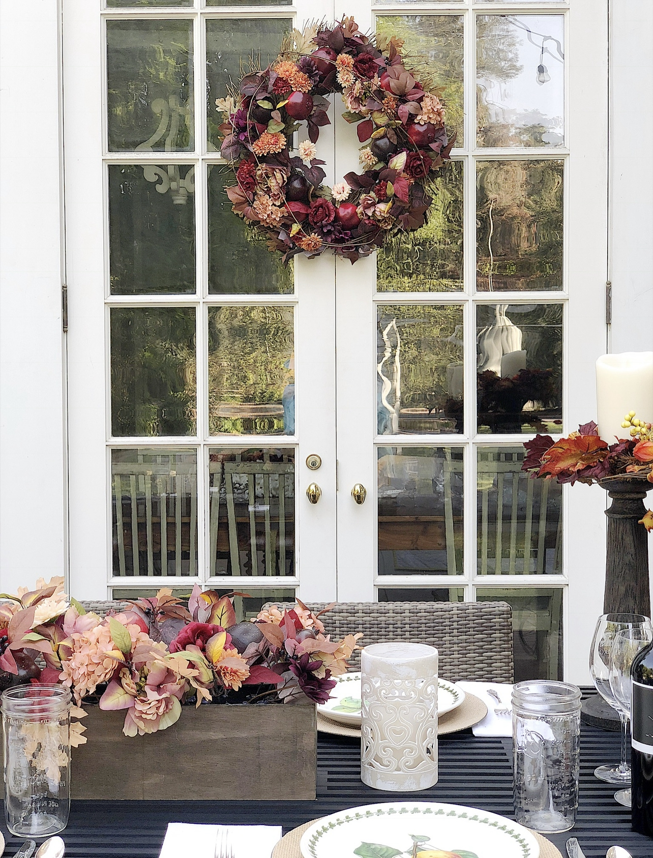 A fall table set on a back porch wtrh gorgeous faux florals, portmeirion plates, and a charcuterie board.