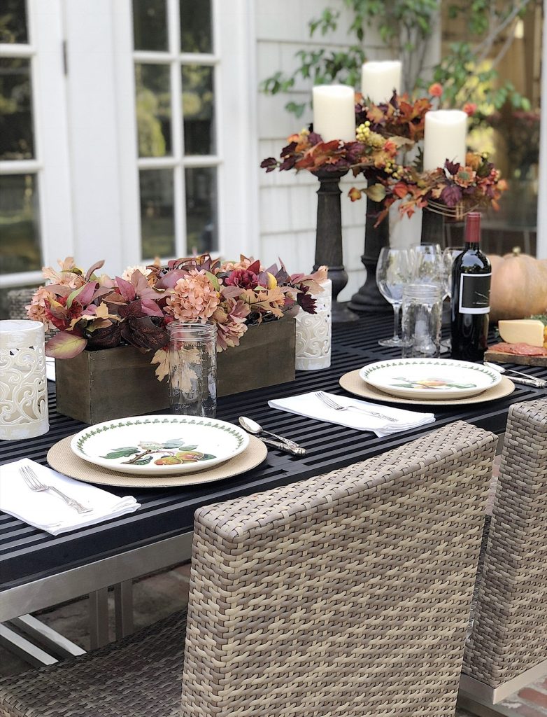 A fall table set on a back porch wtrh gorgeous faux florals, portmeirion plates, and a charcuterie board.