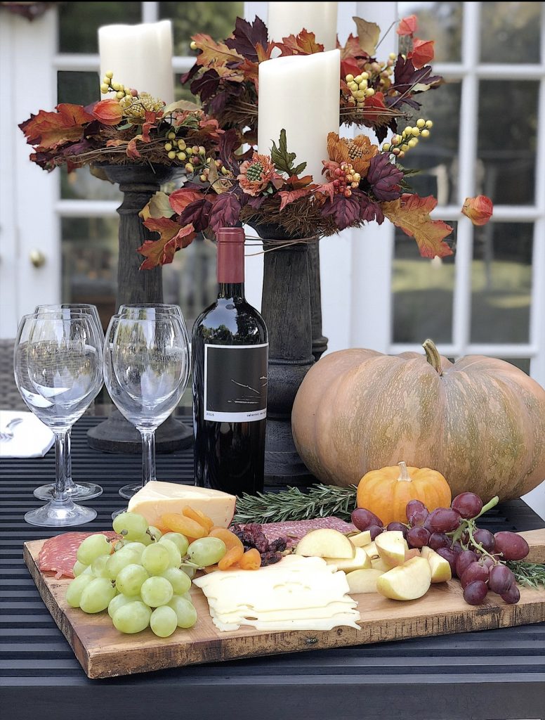 A fall table set on a back porch wtrh gorgeous faux florals, portmeirion plates, and a charcuterie board.