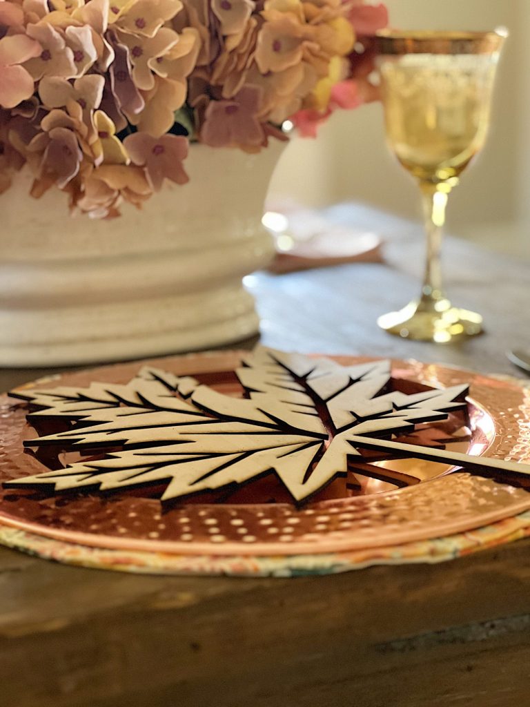 A fall themed table with a placemat, copper charger, amber glassware and a fall leaf wood charger cut with a laser cutting machine.