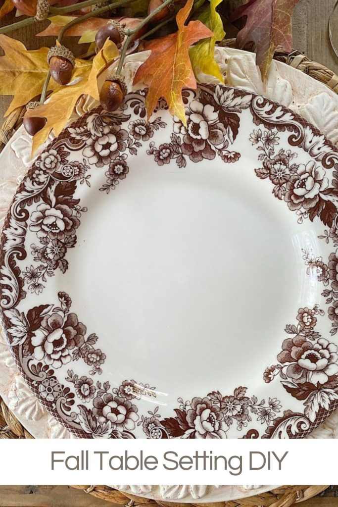 A fall placesetting with a Spode brown and white plate, a homemade leaf charger, and some fall decor leaves.
