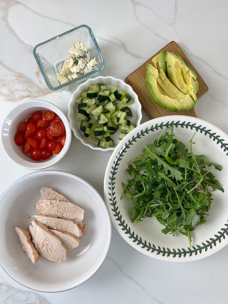 The best chicken protein bowl with arugula, tomatoes, cucumbers, avocado, and gorgonzola.