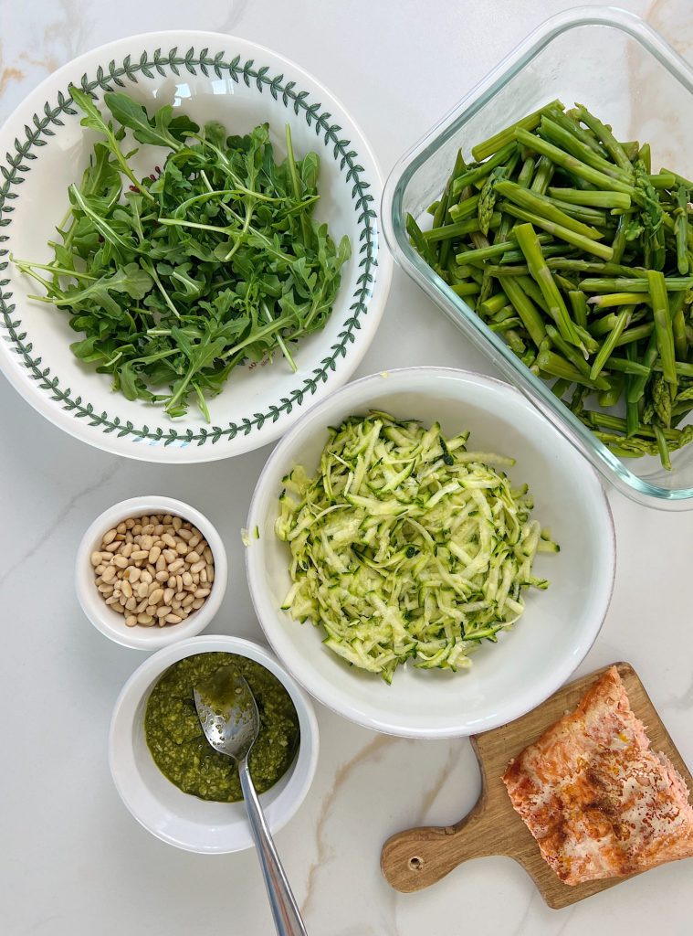 The best salmon protein bowl with arugula, grated zucchii, steamed asparagus, pesto, and pine nuts..