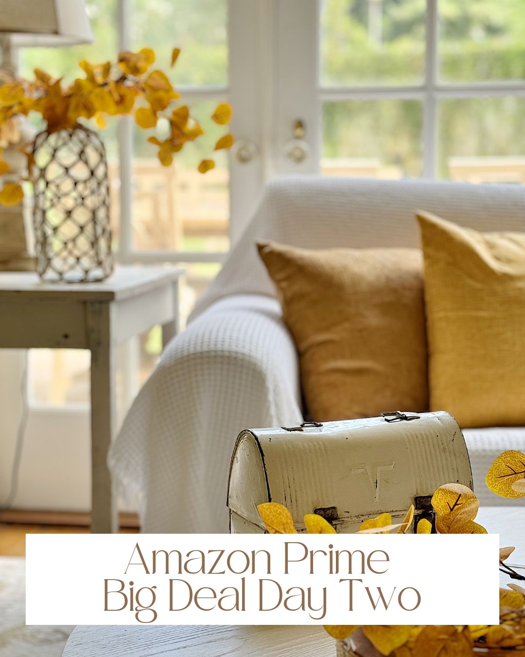 A cozy living room with a white couch and yellow pillows. A decorative table with a vase of yellow flowers is next to it. Text reads "Amazon Prime Big Deal Day Two". Enjoy exclusive offers on your favorite home decor items with Amazon Prime!