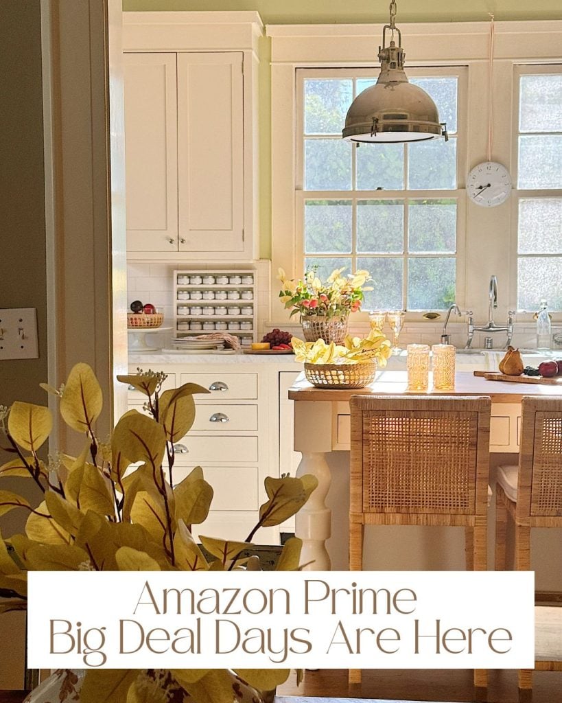 A cozy kitchen with wicker stools, fruit baskets, and plants lit by a pendant lamp. Text overlay at the bottom reads, "Amazon Prime Big Deal Days Are Here.