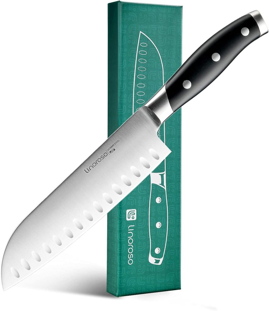 A stainless steel santoku knife with a black handle, perfect for preparing fall soup recipes, is elegantly displayed alongside its green packaging box.