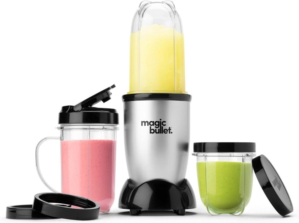 Magic Bullet blender with three cups brimming with yellow, pink, and green smoothies, alongside additional lids and a hint of purple sweet potato goodness.