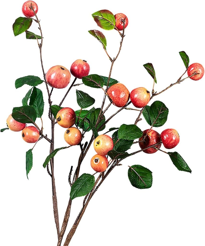 Artificial branches with red apples and green leaves are artfully arranged against a white background, evoking the cozy warmth of a fall blanket.