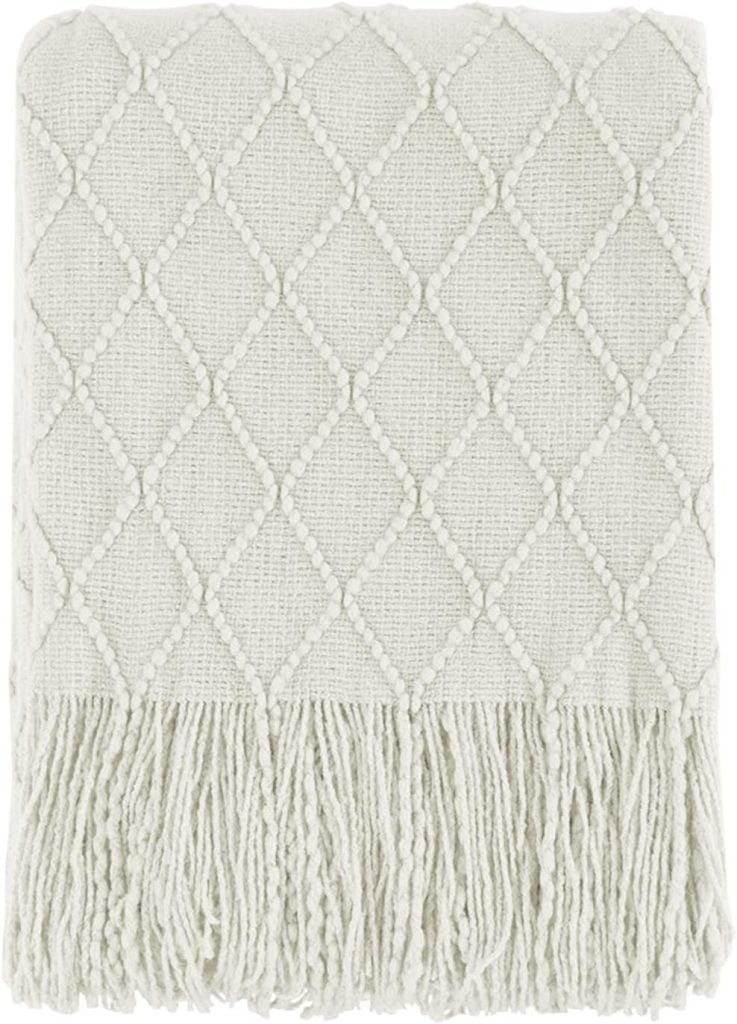 A cozy folded fall blanket in textured cream, featuring a diamond pattern and fringe on the edges.