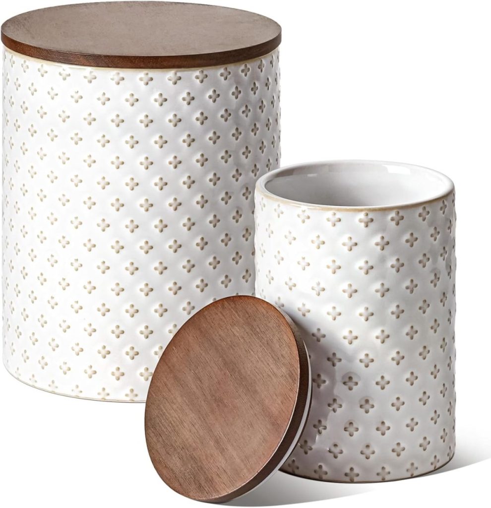 Two white ceramic canisters with small cross patterns, one standing with a closed wooden lid, and the other with an open lid placed next to it—perfect for storing your freshly baked pumpkin banana bread.