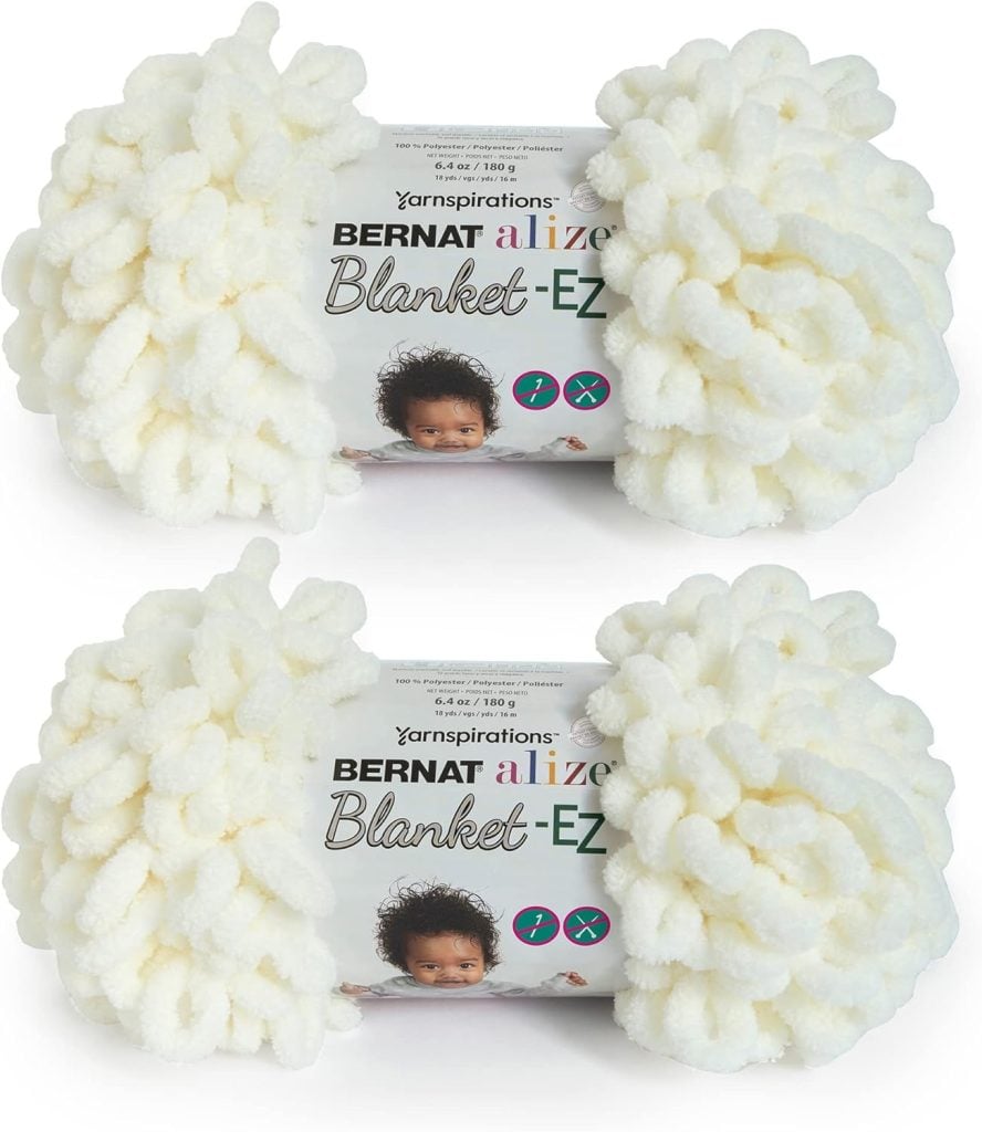 Two skeins of Bernat Alize Blanket-EZ yarn in white, each adorned with a label featuring a baby. Perfect for crafting a cozy fall blanket, the label provides details on weight and length, ensuring the ideal project for cooler days.