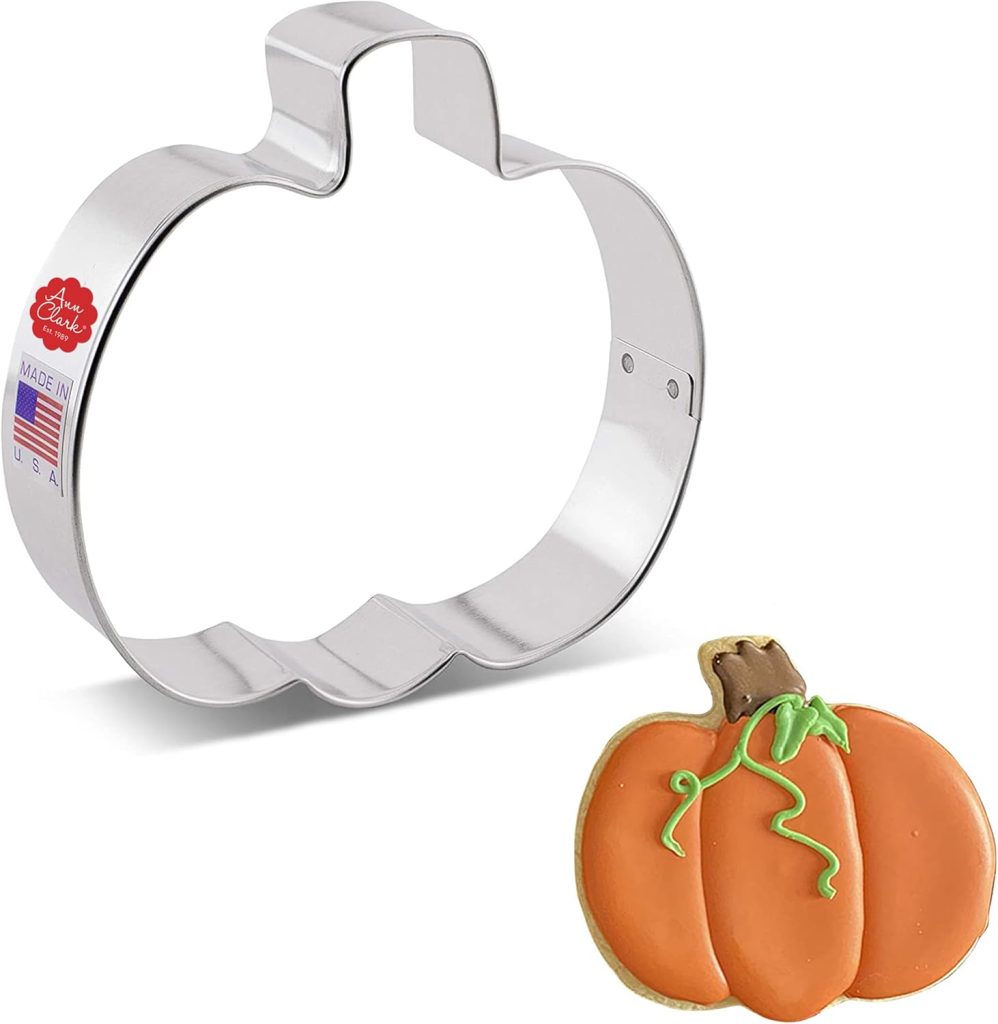 A metal pumpkin-shaped cookie cutter is shown alongside a delightful Halloween sugar cookie, decorated with green icing.