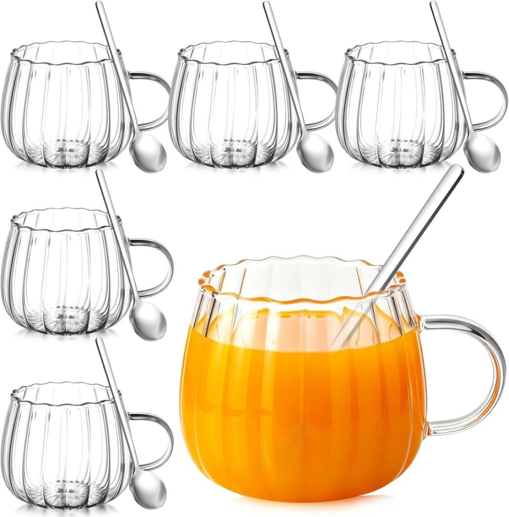 Six clear glass mugs with vertical grooves, each paired with a metal spoon; one mug is filled with orange liquid and has a spoon inside, perfect for enjoying your favorite pumpkin trifle recipe.