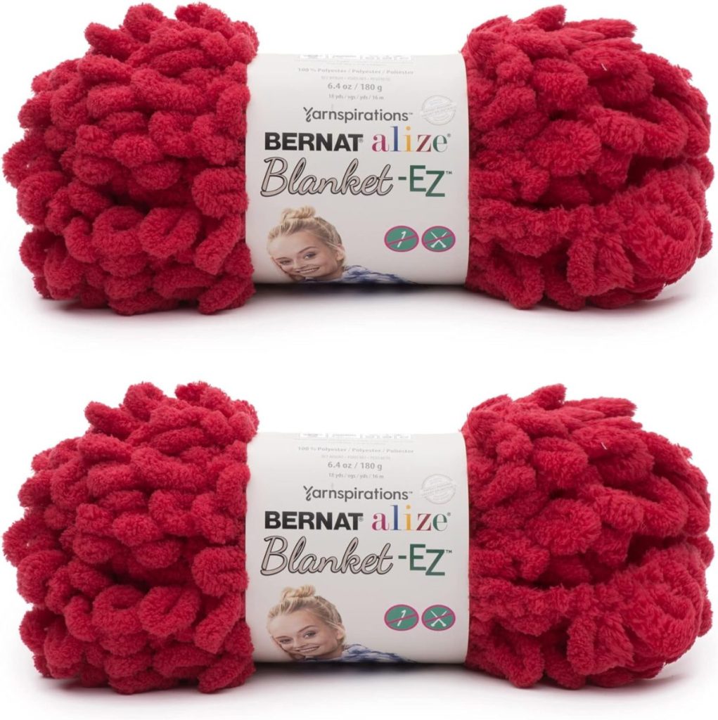 Two skeins of red Bernat Alize Blanket-EZ yarn, perfect for crafting a cozy fall blanket, with labels showing product details and a picture of a woman.