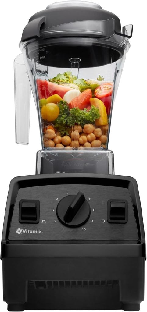 A black Vitamix blender brimming with chickpeas, kale, cherry tomatoes, and purple sweet potato sits elegantly against a plain background.