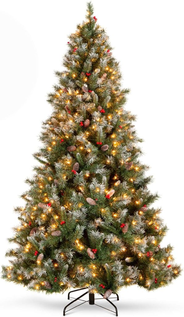 A decorated Christmas tree with lights, pinecones, and red berries, standing on a metal stand against a plain background, evokes the warmth of Halloween sugar cookies freshly out of the oven.