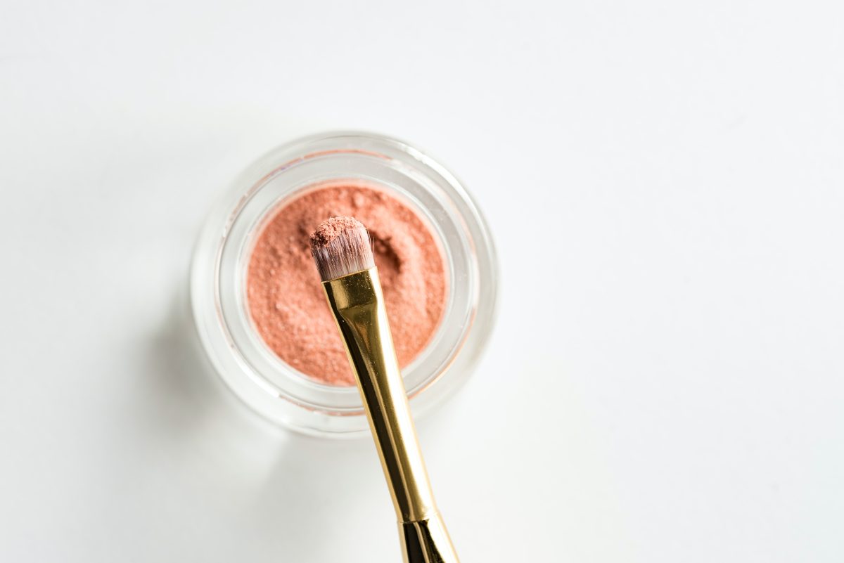 a small jar with pink makeup and a makeup brush