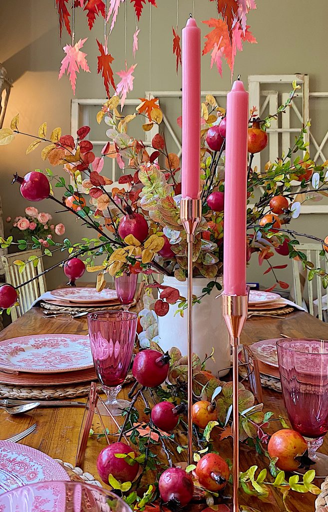 A beautiful fall table with orange and pink candles, faux flowers, and homemade painted and cut leaves.