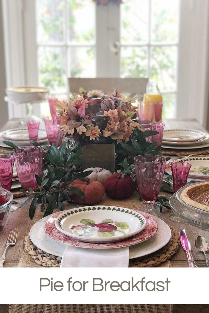 A table set for breakfast with cranberry glasses and plates, and a centerpiece. It's set to enjoy pice for breakfast on the day after Thanksgiving.